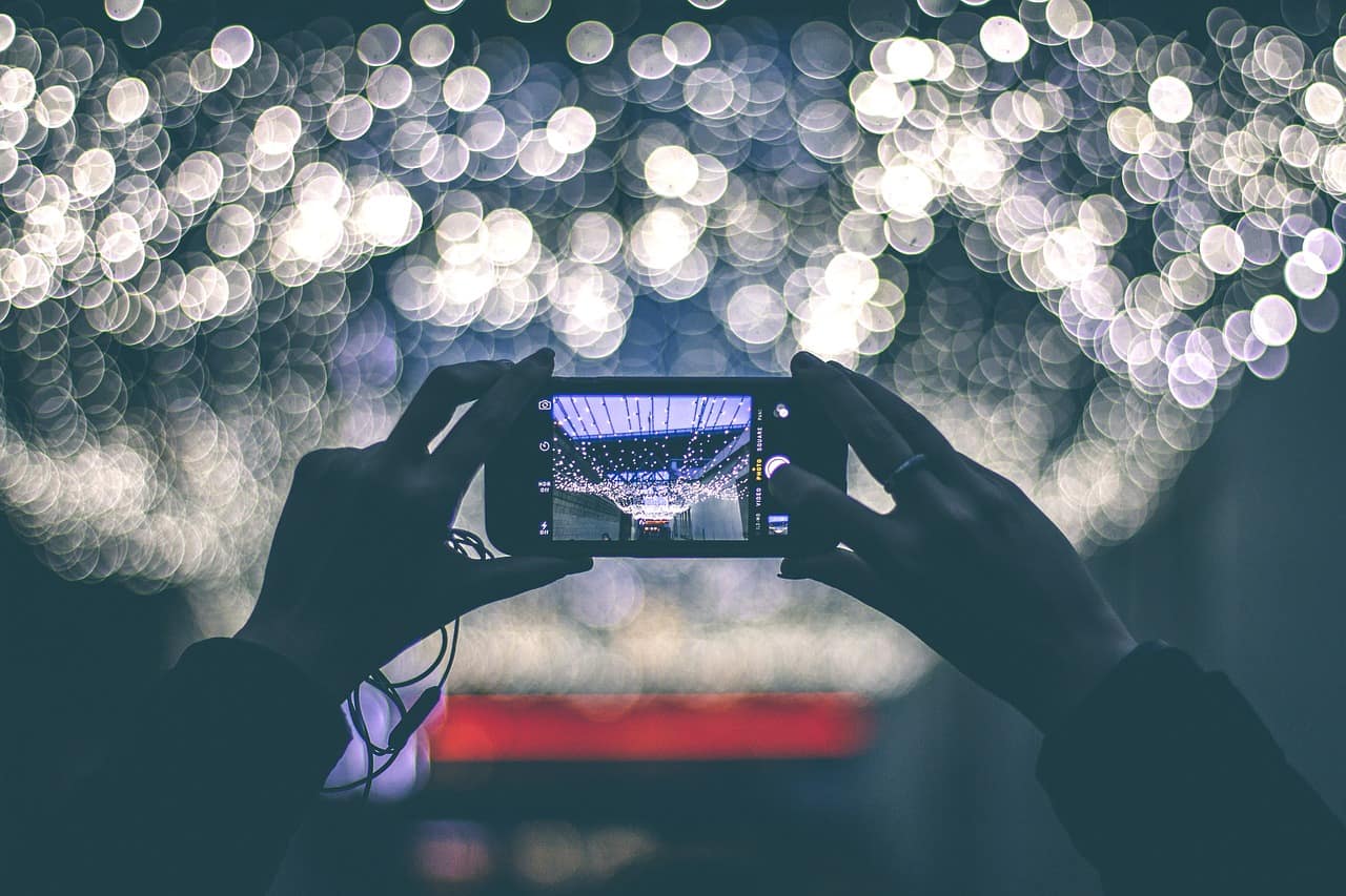 Mobile phone being held up by 2 hands with lights in background portraying impact of visuals in digital marketing